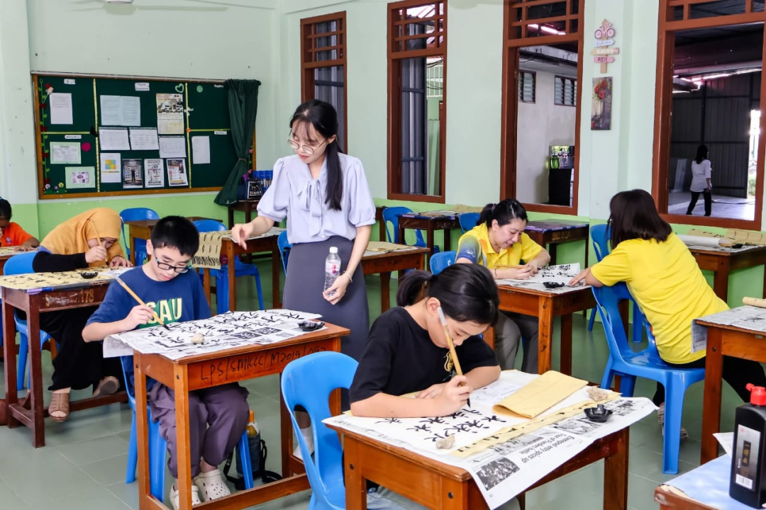 教室内，学生使用毛笔作画，教师站在桌旁指导。